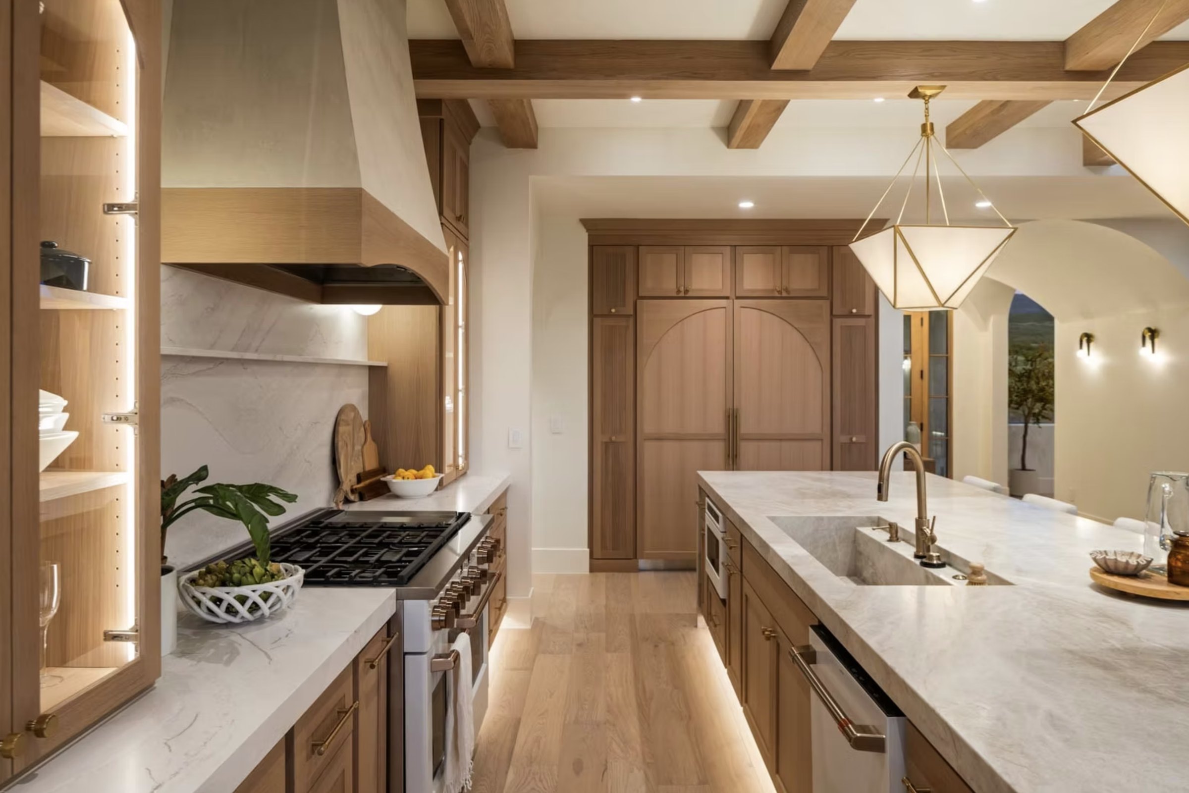 Warm modern kitchen with white oak cabinetry, a plaster hood, marble counters and a beamed ceiling